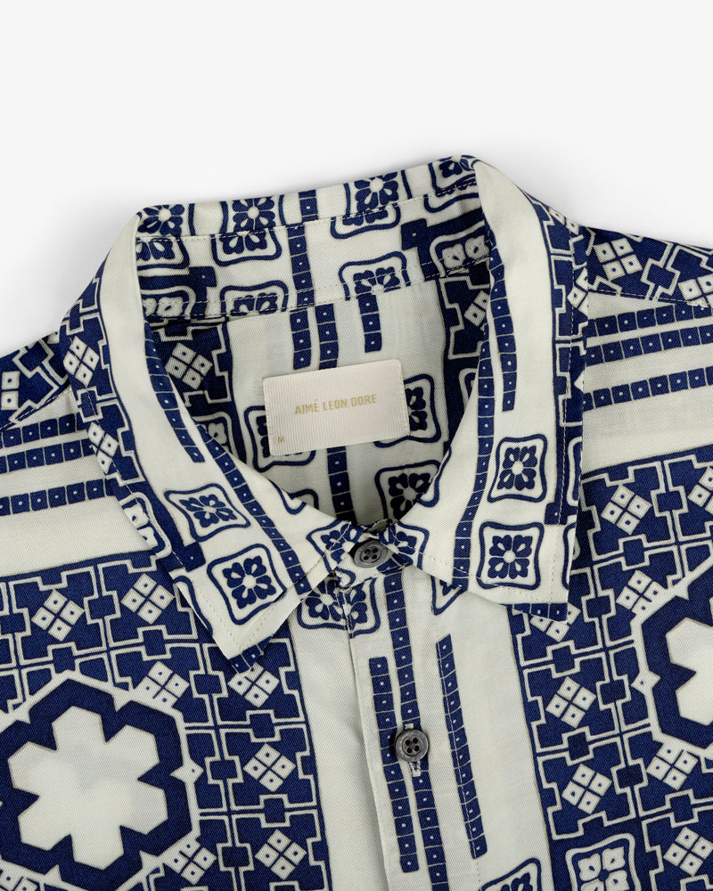 Close-up of the Mosaic Button Down Shirt with a blue and white geometric pattern and buttons, Aimé Leon Dore label inside.