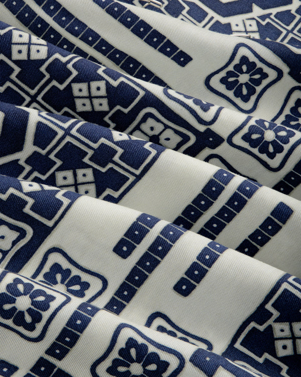 The Mosaic Button Down Shirt features white fabric with blue geometric and floral patterns, shown with gentle folds.