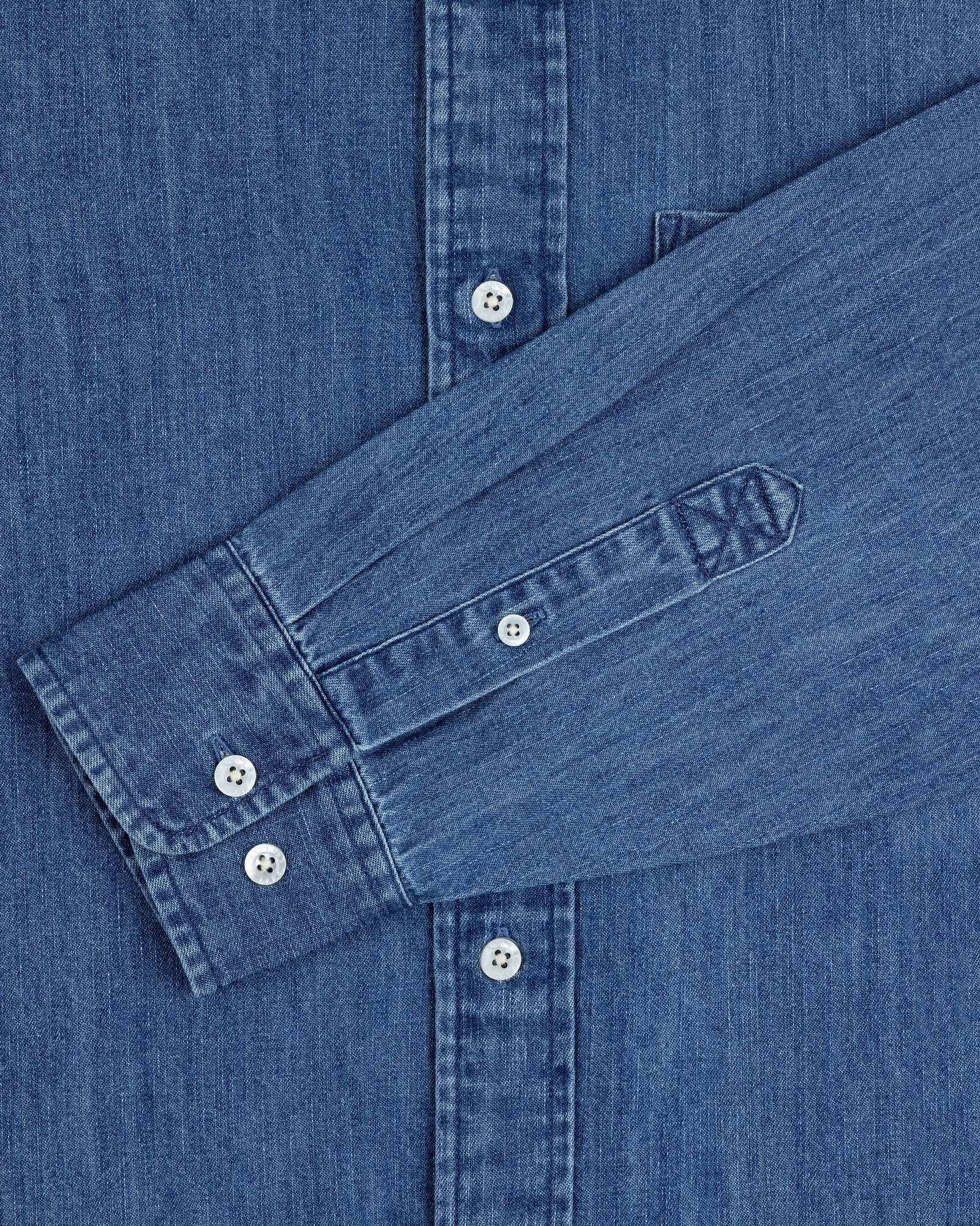 A close-up of the Crest Chambray Shirt in blue with one sleeve laid across the front.