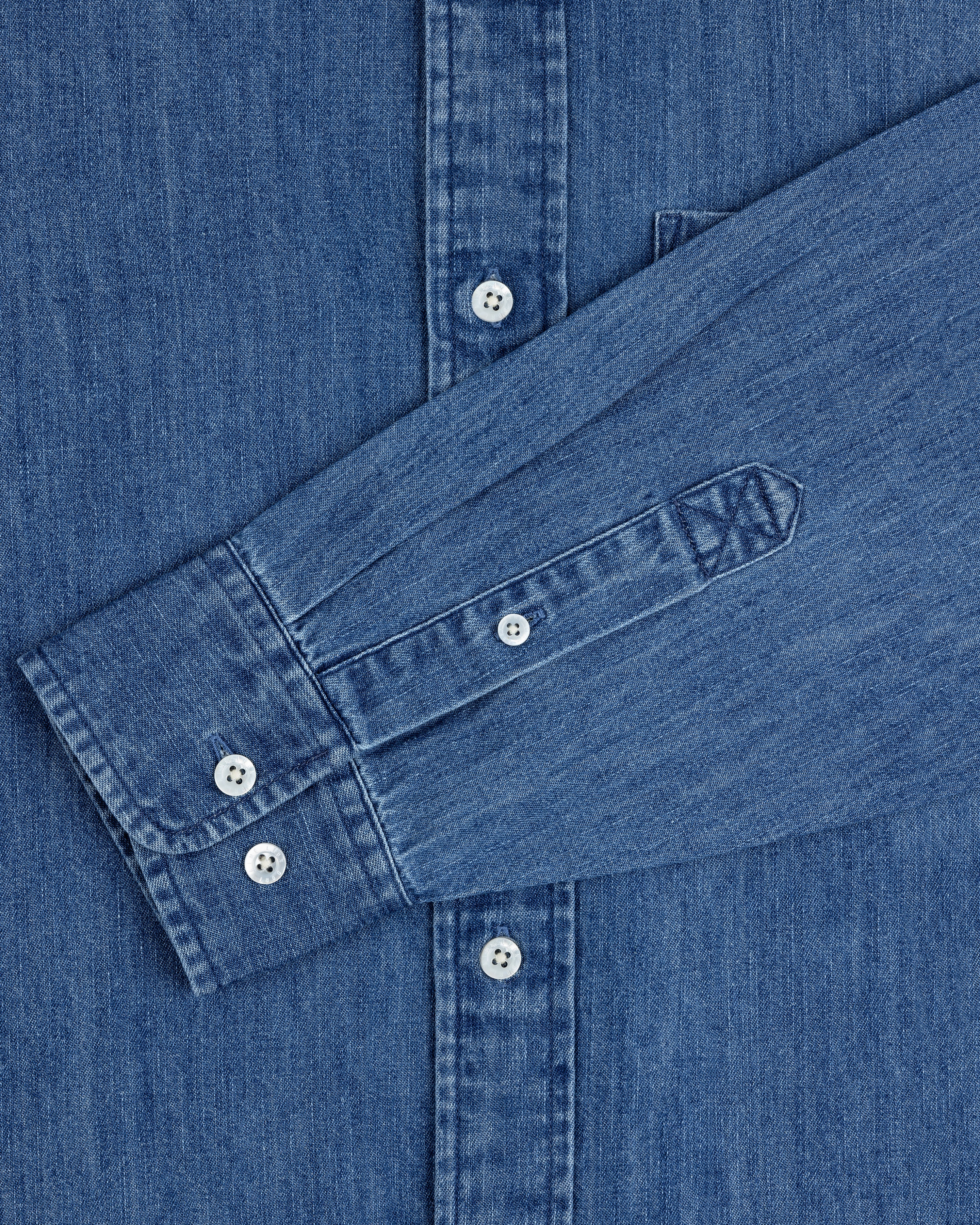 A close-up of the Crest Chambray Shirt in blue with one sleeve laid across the front.