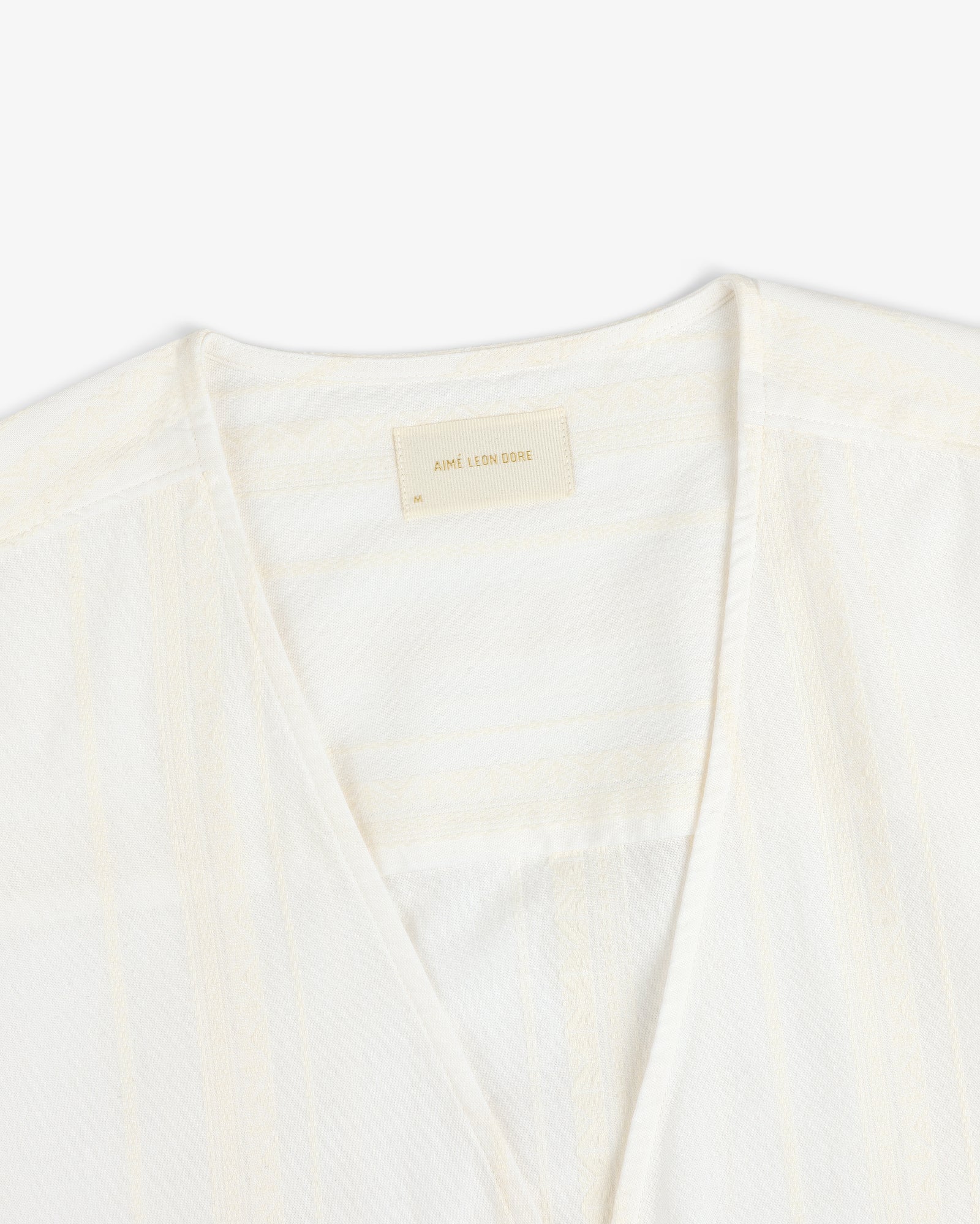 Close-up of the Jacquard Striped Tie-Front Shirt, cream-colored with subtle patterns and a beige Aimé Leon Dore label.