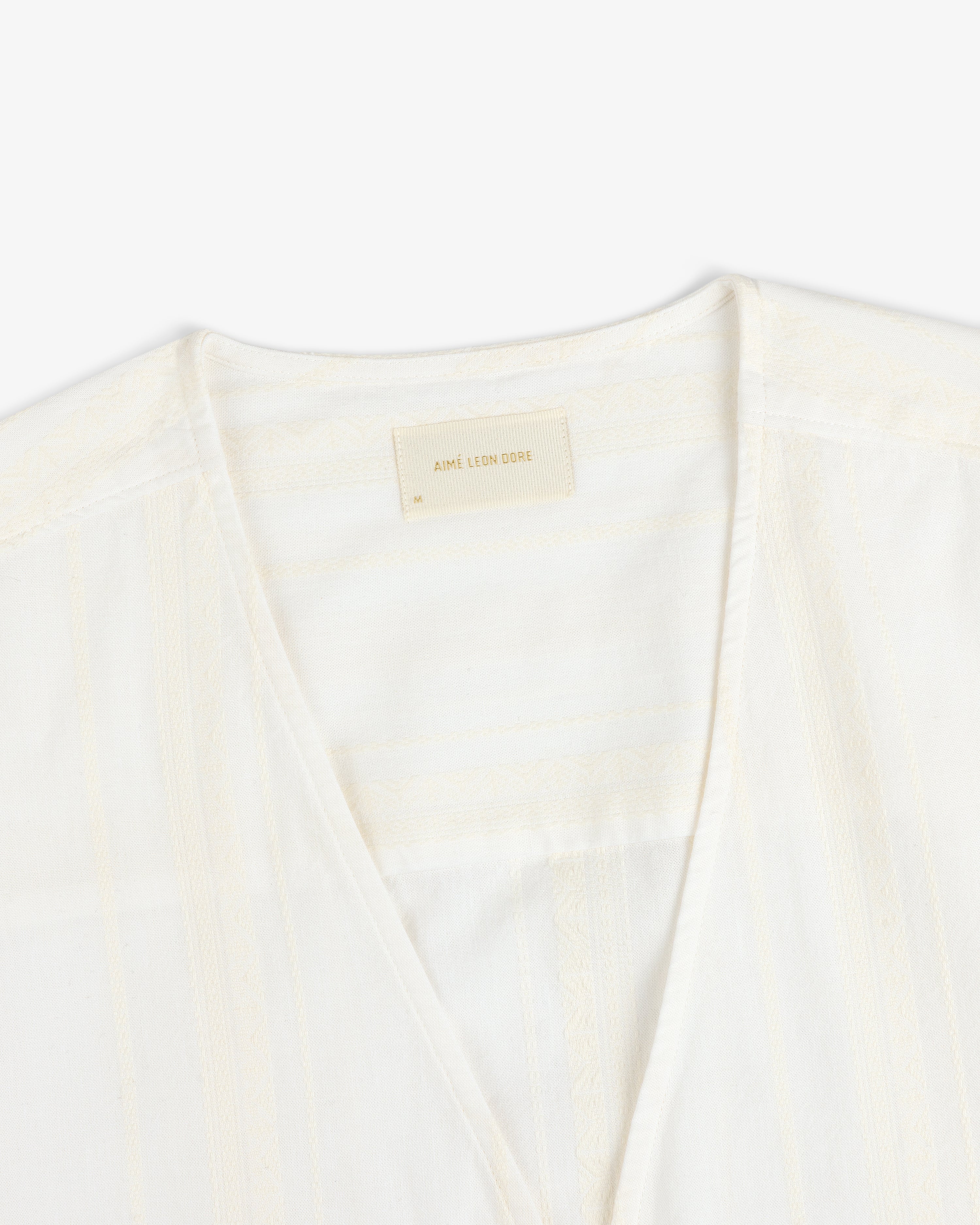 Close-up of the Jacquard Striped Tie-Front Shirt, cream-colored with subtle patterns and a beige Aimé Leon Dore label.