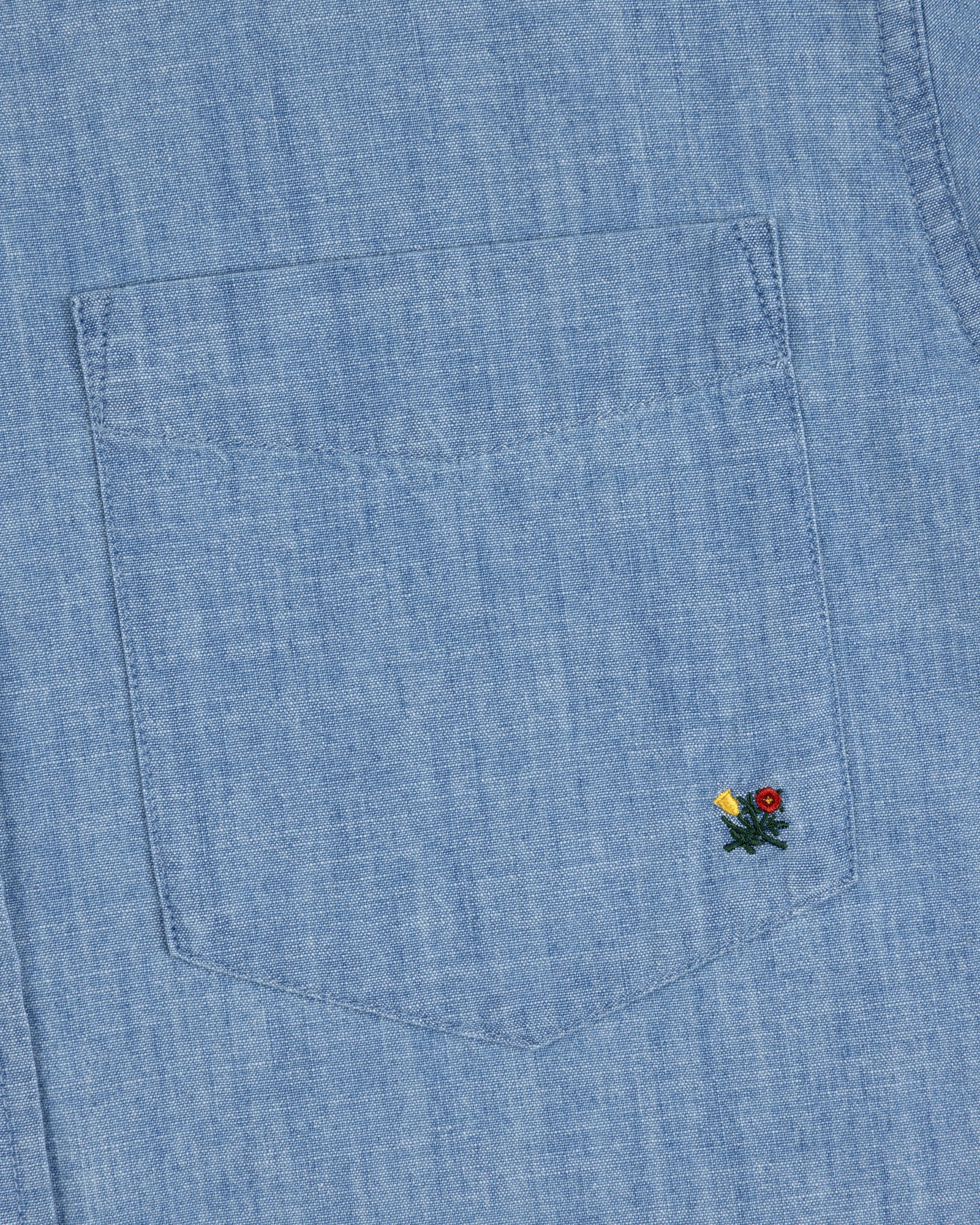 Close-up of the Crest Chambray Shirt’s blue denim pocket with yellow and red flower embroidery at the bottom right.