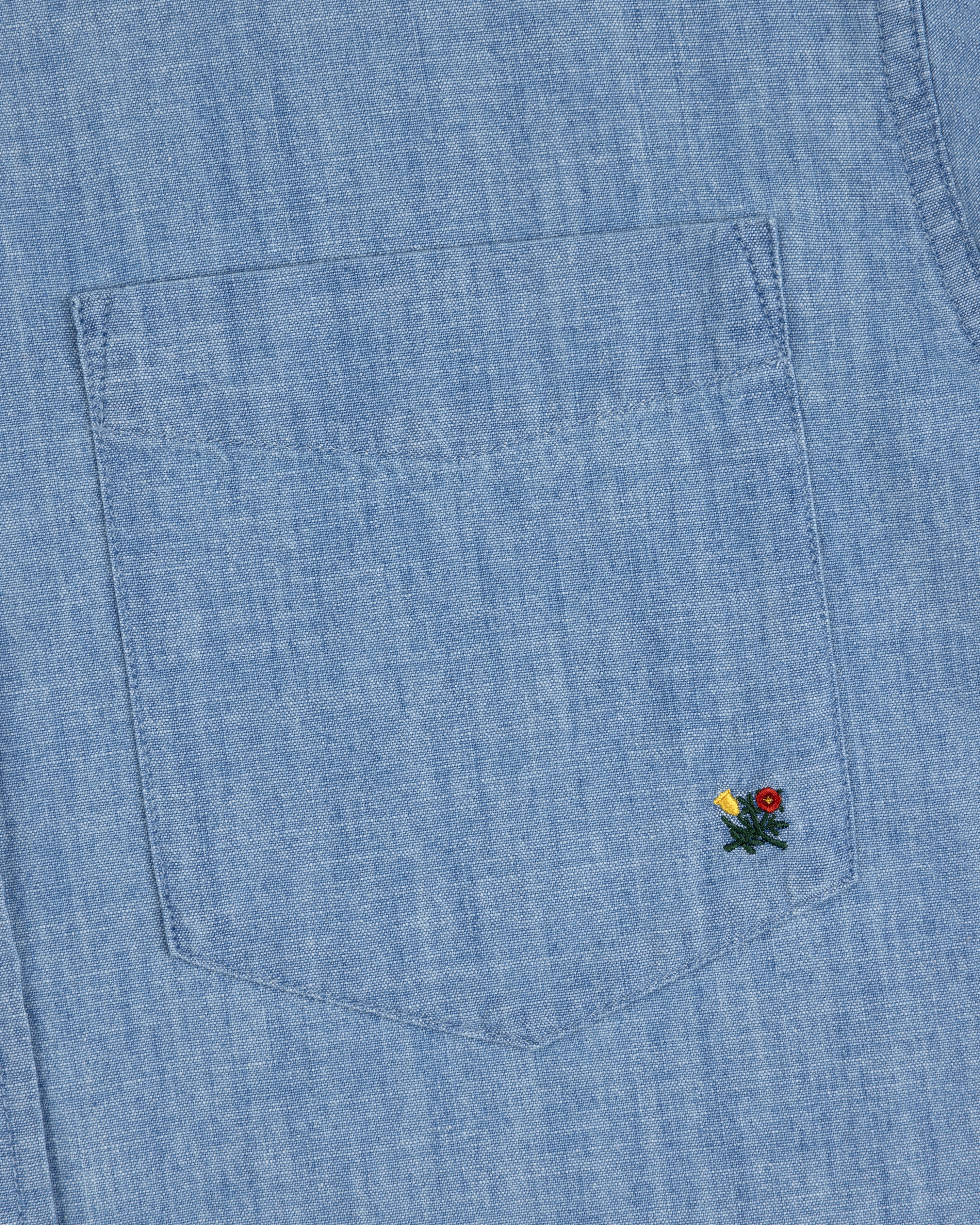 Close-up of the Crest Chambray Shirt’s blue denim pocket with yellow and red flower embroidery at the bottom right.