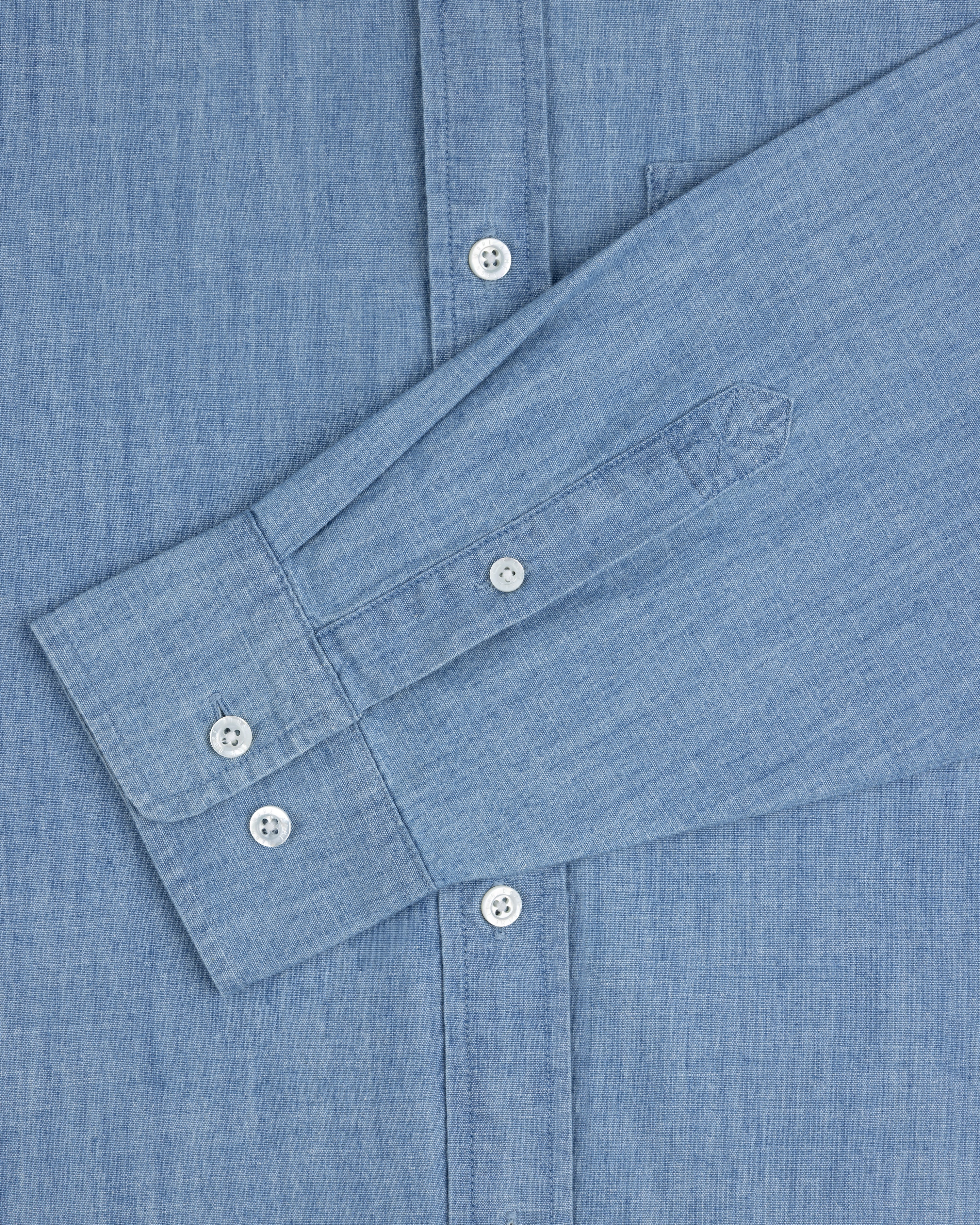 Crest Chambray Shirt in light blue with white buttons, featuring long sleeves laid flat across the front.