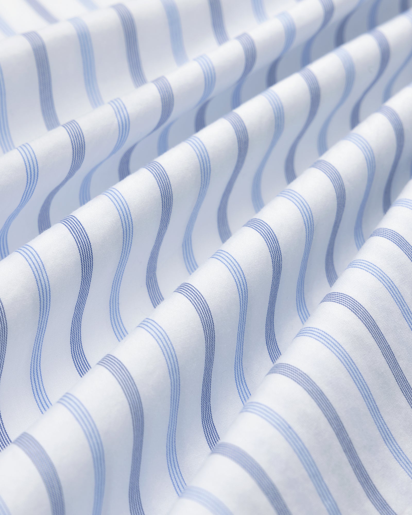 Close-up of Poplin Casual Shirt fabric with wavy blue and light blue stripes in soft, diagonal folds.