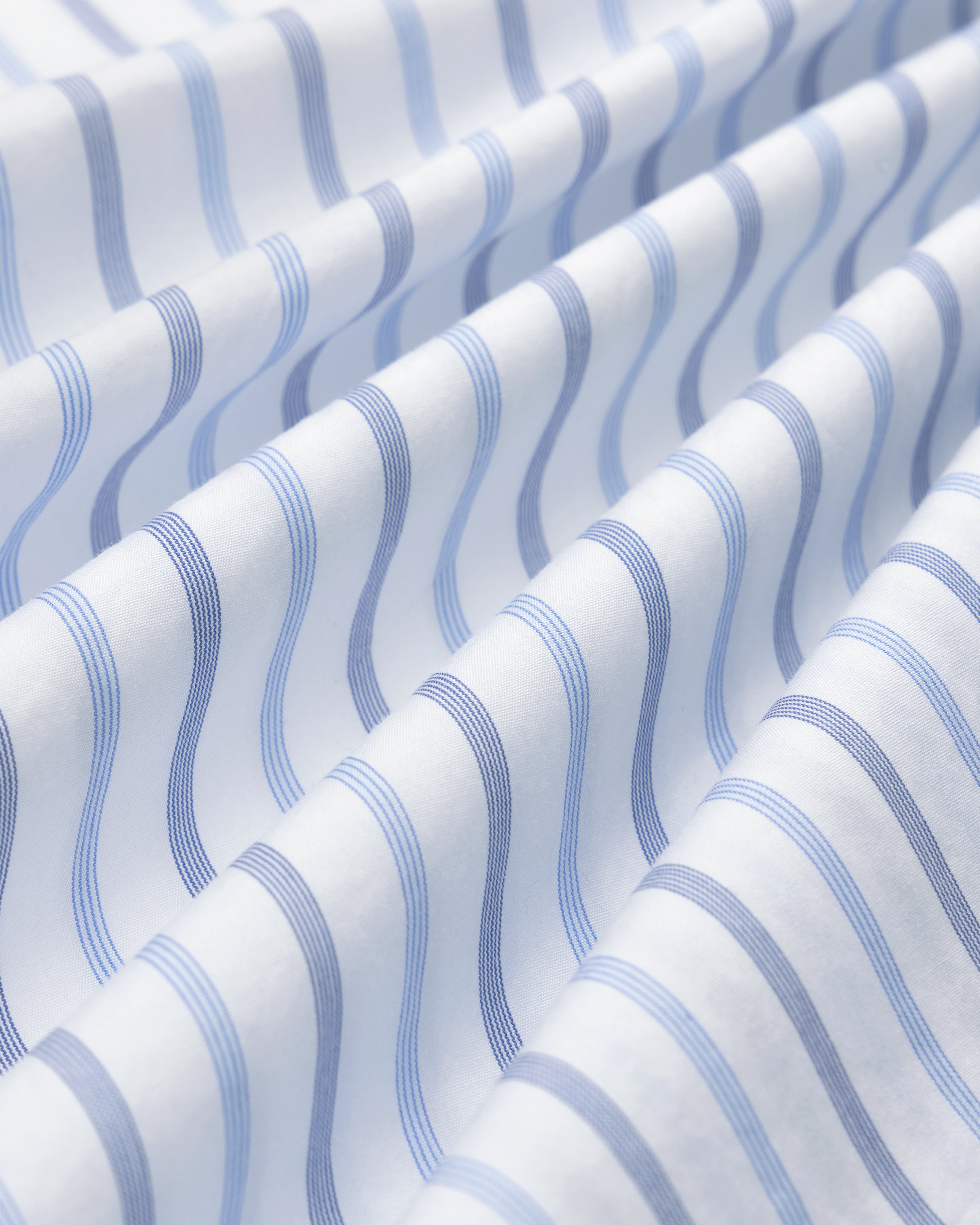 Close-up of Poplin Casual Shirt fabric with wavy blue and light blue stripes in soft, diagonal folds.