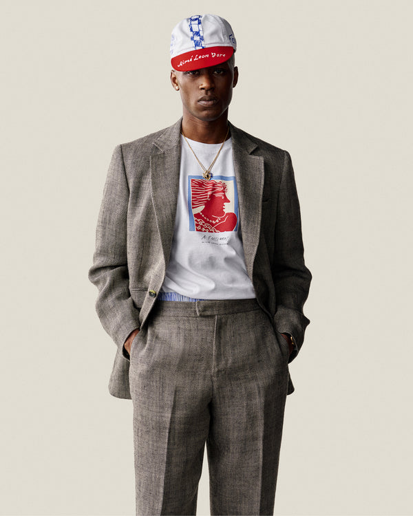 Man in gray suit, Fassianos Portrait Tee, and white-red baseball cap stands with hands in pockets.