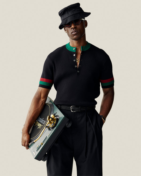 A stylish man in black sunglasses and hat holds a portable turntable, wearing the Sport Knit Henley.