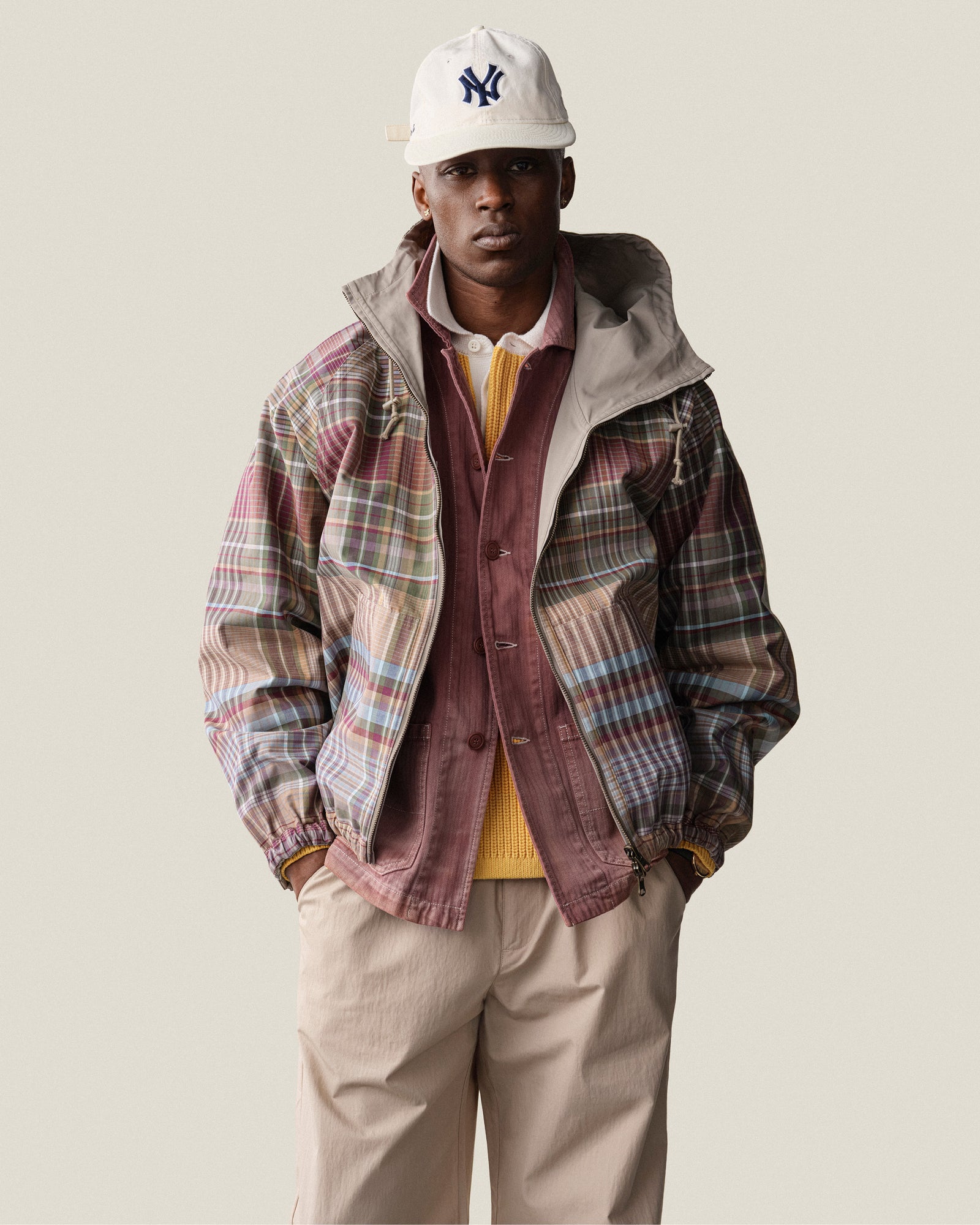 A man wears the Reversible Madras Windbreaker over a yellow sweater, beige pants, and a white baseball cap.
