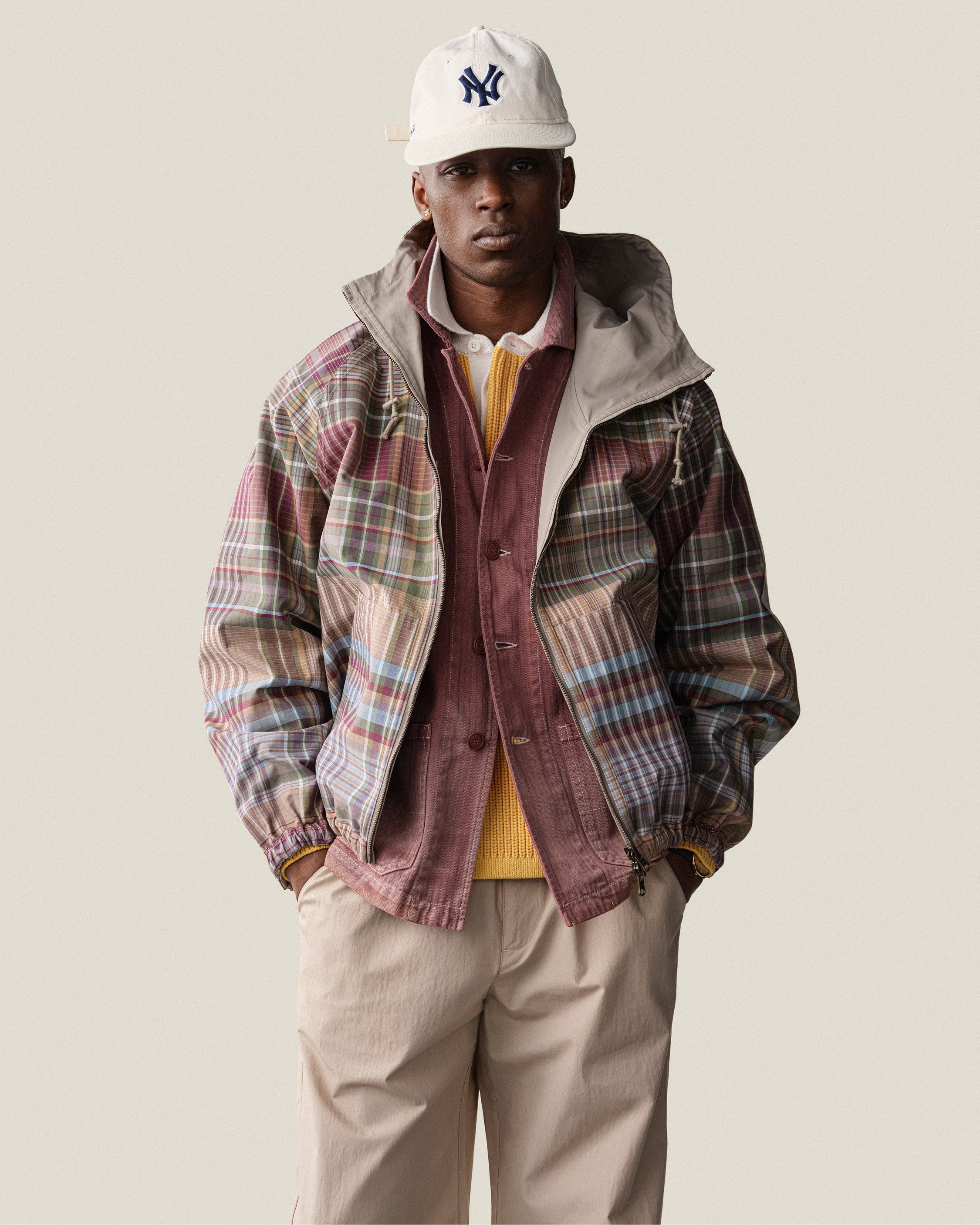 A man wears the Reversible Madras Windbreaker over a yellow sweater, beige pants, and a white baseball cap.