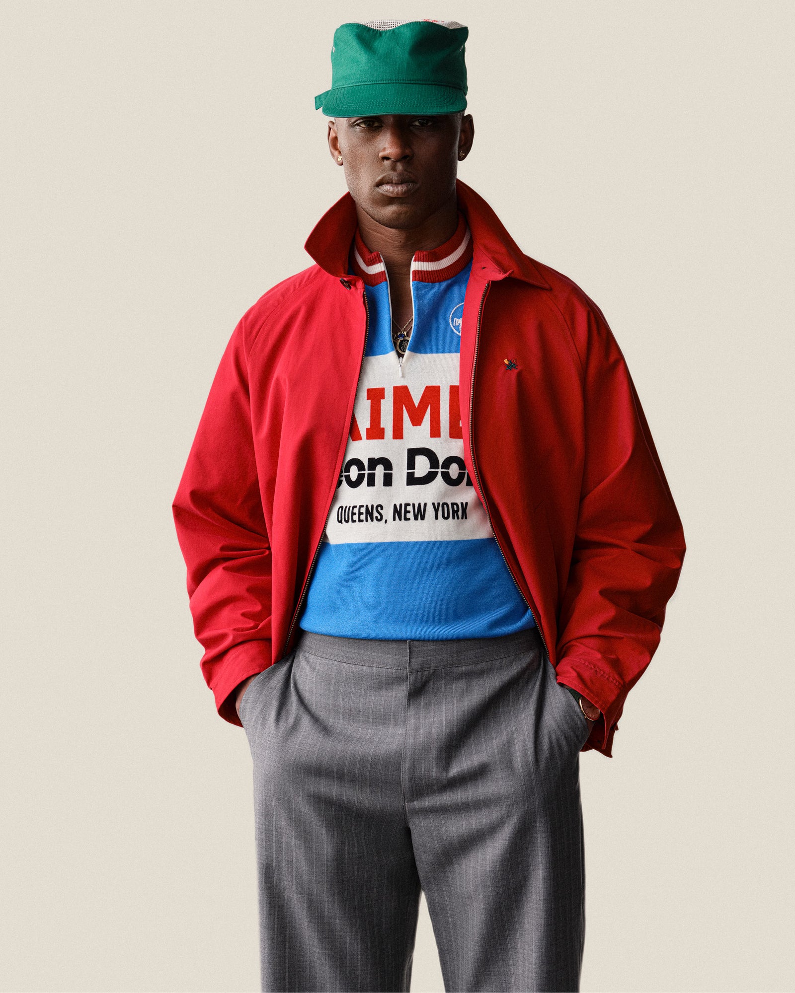 Man in Merino Wool Cycling Jersey, gray pants, and green cap stands with hands in pockets.