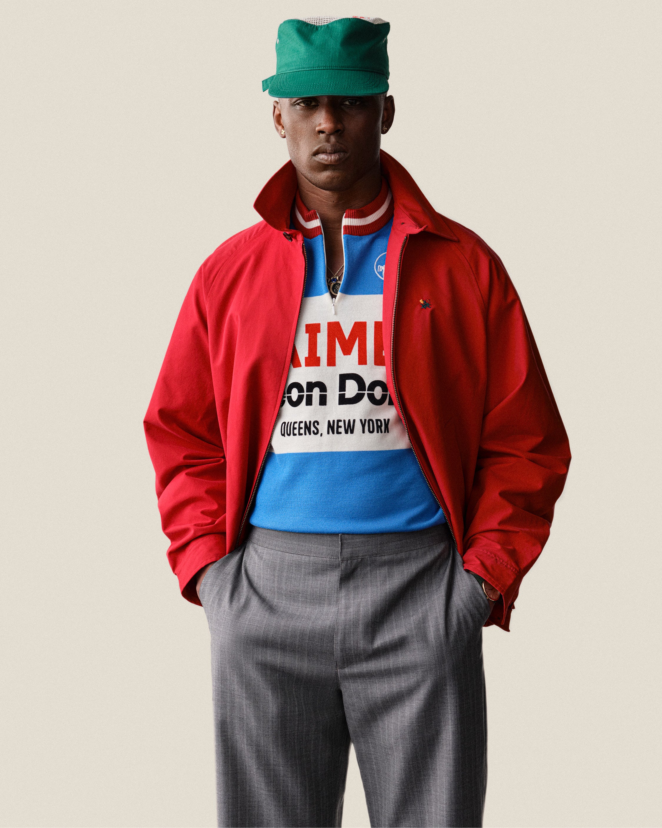 Man in Merino Wool Cycling Jersey, gray pants, and green cap stands with hands in pockets.