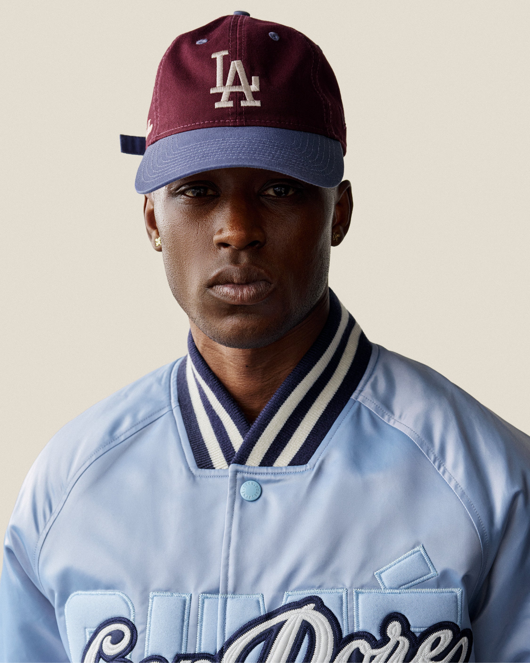 A person wears the ALD / LA Dodgers Colorblock Ballpark Hat and a light blue varsity jacket, facing the camera.