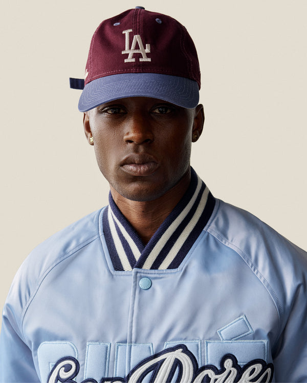 A person wears the ALD / LA Dodgers Colorblock Ballpark Hat and a light blue varsity jacket, facing the camera.