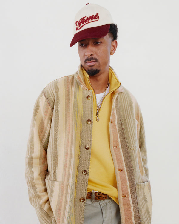 Man wearing a Cycling Logo Hat, striped jacket, and yellow shirt, looking to the side against a plain background.