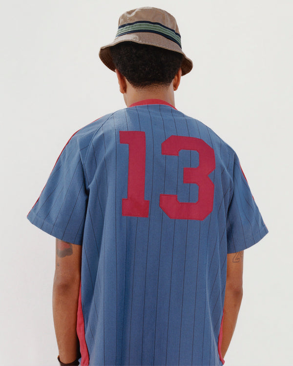 Person facing away in a Crest Bucket Hat and blue pinstriped shirt with red number 13 on the back.