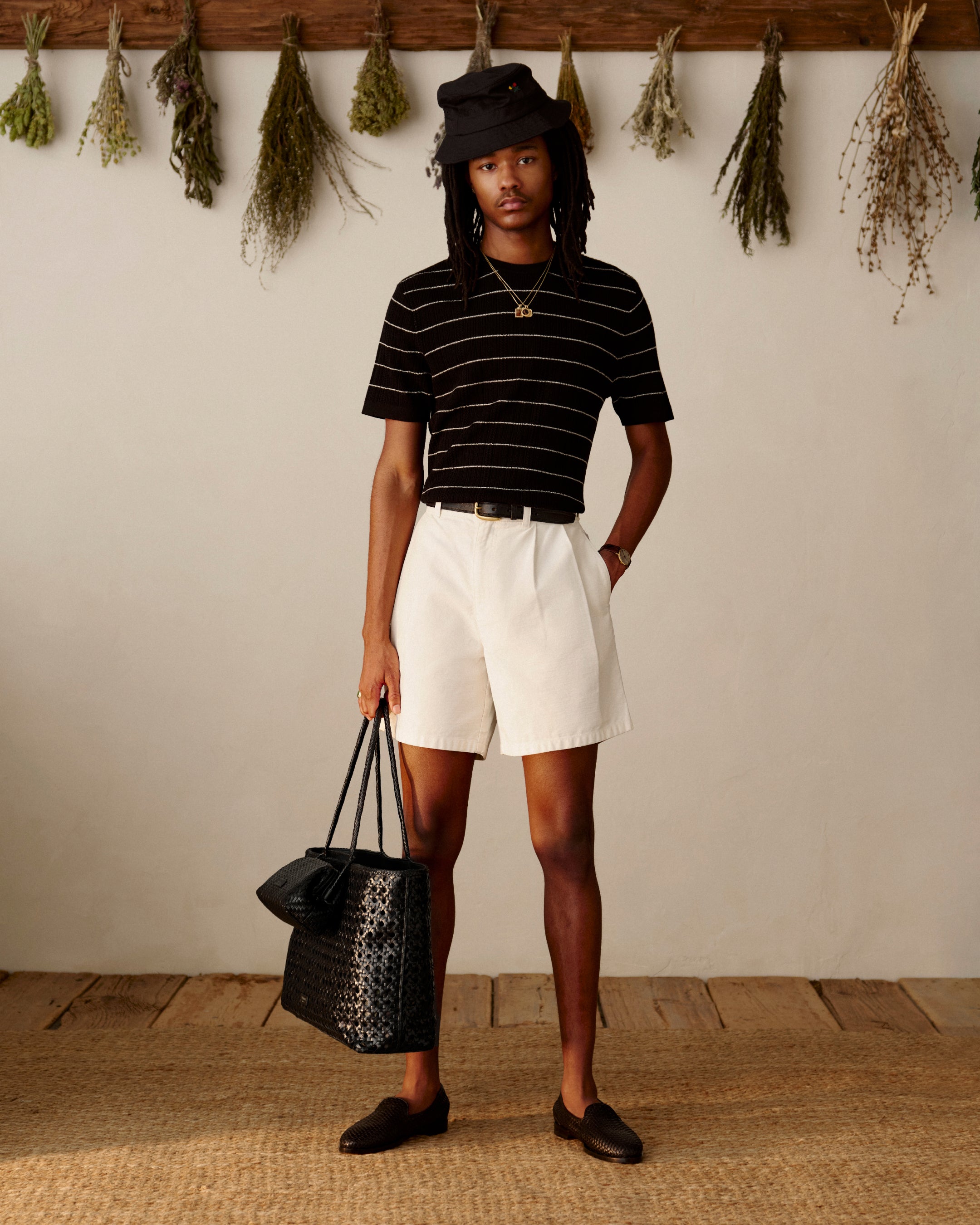 A person in a striped shirt and loafers holds a Woven Leather Shoulder Bag, standing indoors.