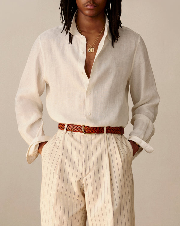 Person wearing a Long-Sleeve Linen Shirt, striped high-waisted trousers, and a brown belt, hands in pockets.