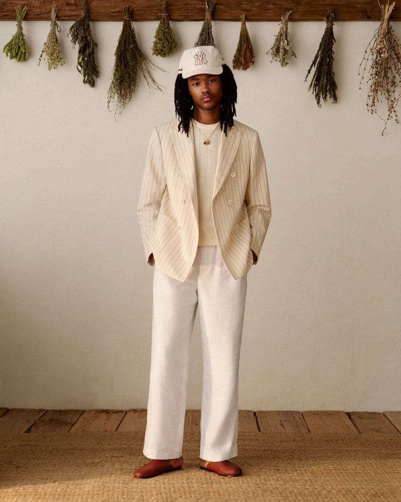 Wearing a cream suit and white shirt, a person indoors sports an ALD / New York Yankees Retro Fit Hat.