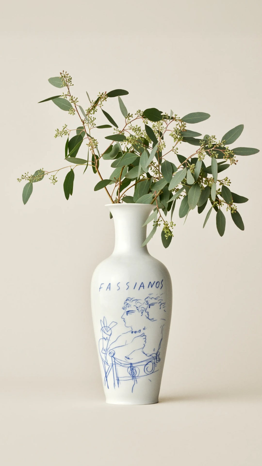 White vase with blue design and eucalyptus leaves on a beige background.