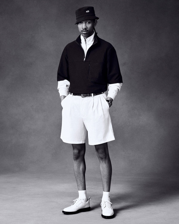 Man in an ALD Golf Quarter Zip Pullover, white shirt, shorts, socks, and shoes poses against a plain backdrop.