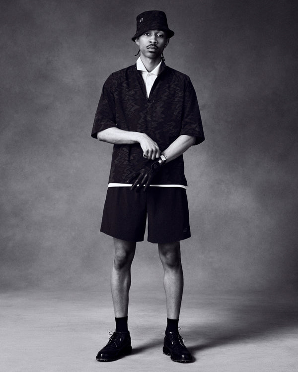 A man in a bucket hat, dark shirt, and shorts showcases the ALD / Footjoy Croc-Embossed Premiere Series Marquis.