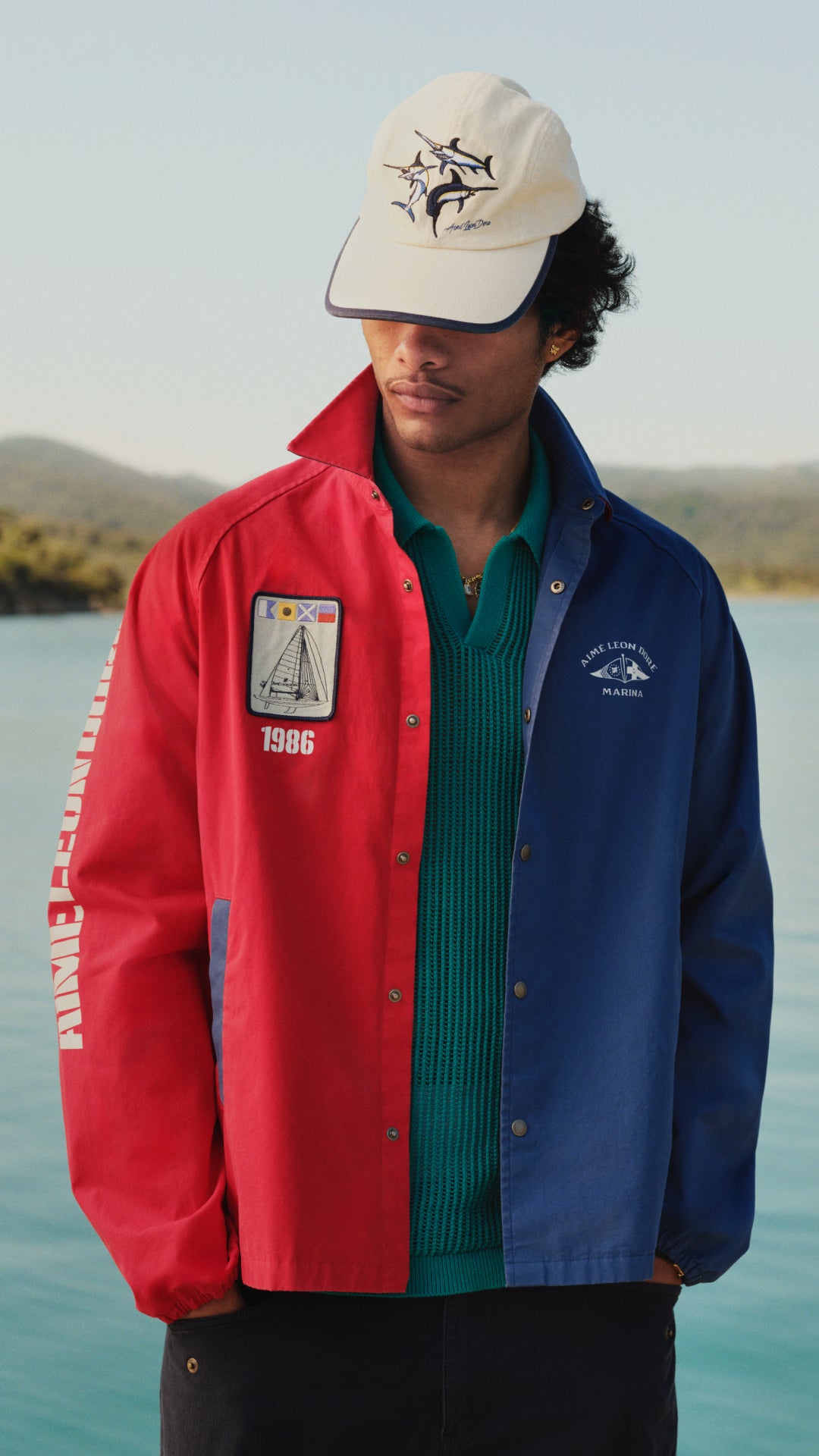 man wearing a jacket and hat in front of the water