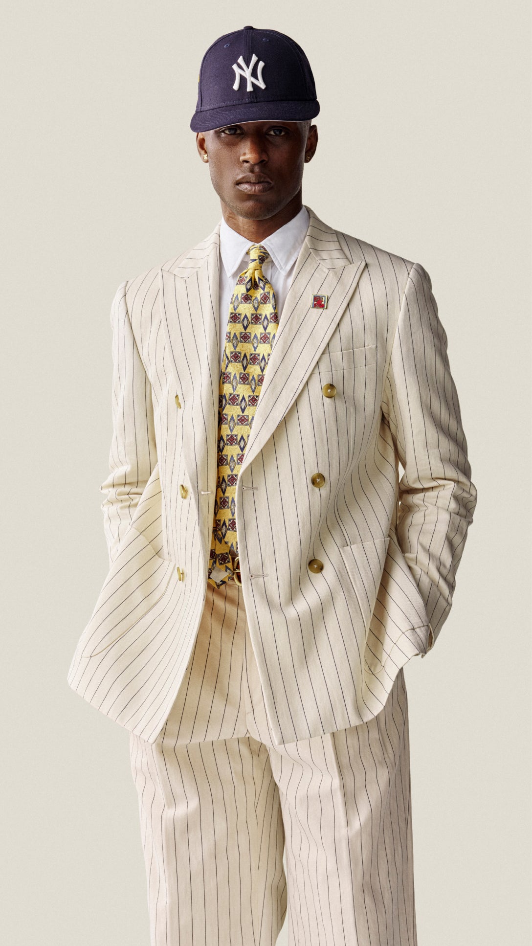 Man wearing a striped suit with a colorful tie and New York Yankees cap on a plain background