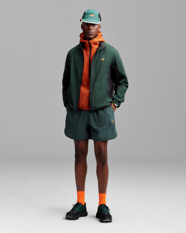 Person wears ALD / New Balance Performance Lightweight Running Short, green jacket, and hat against a gray background.