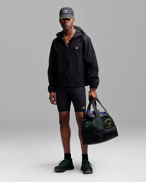 A person wears the ALD / New Balance Breathable Half-Zip Pullover while holding a green duffel bag against a plain background.
