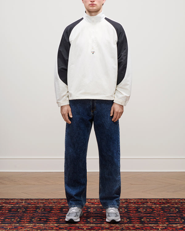 Person stands on patterned rug wearing blue Relaxed Fit 5-Pocket Denim Pant, white and black shirt, and gray sneakers.