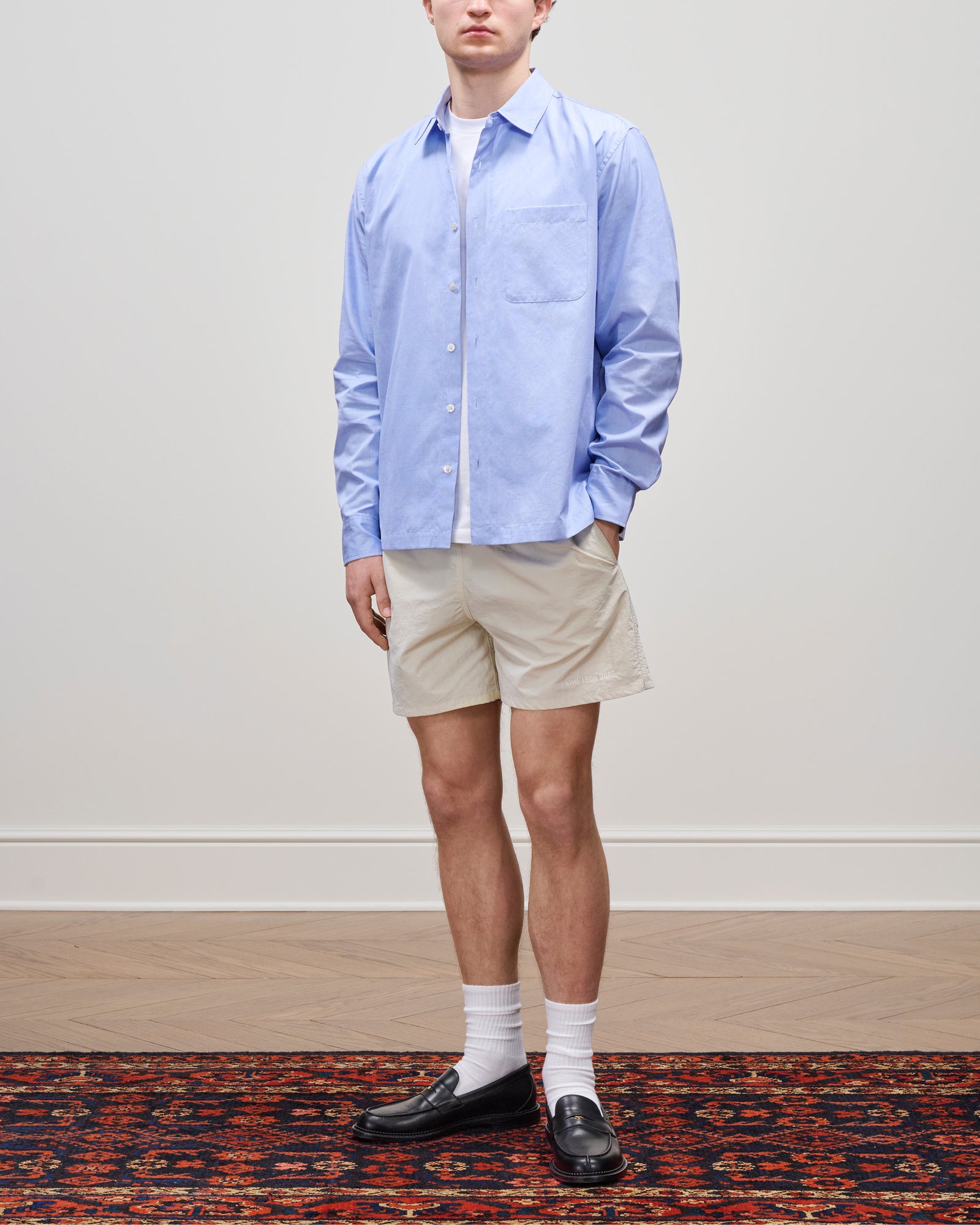 Someone in a Poplin Casual Shirt, beige shorts, white socks, and black loafers stands on a patterned rug.