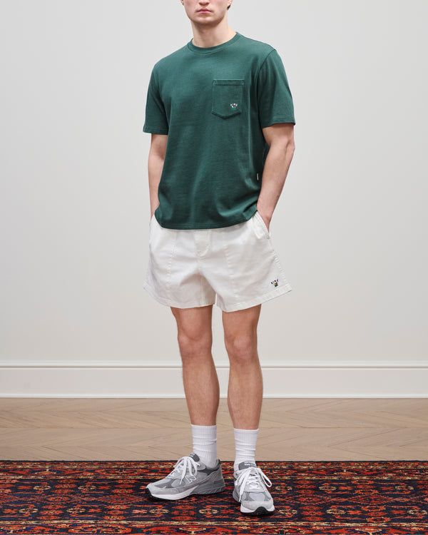 A man wearing a green pocket tee, Crest Casual Short, gray sneakers, and white socks stands on a patterned rug.