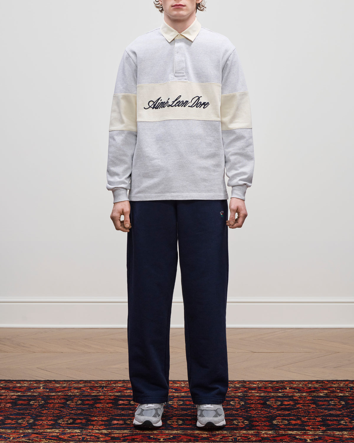 Person wearing the Script Paneled Rugby, navy pants, and grey sneakers, standing indoors.