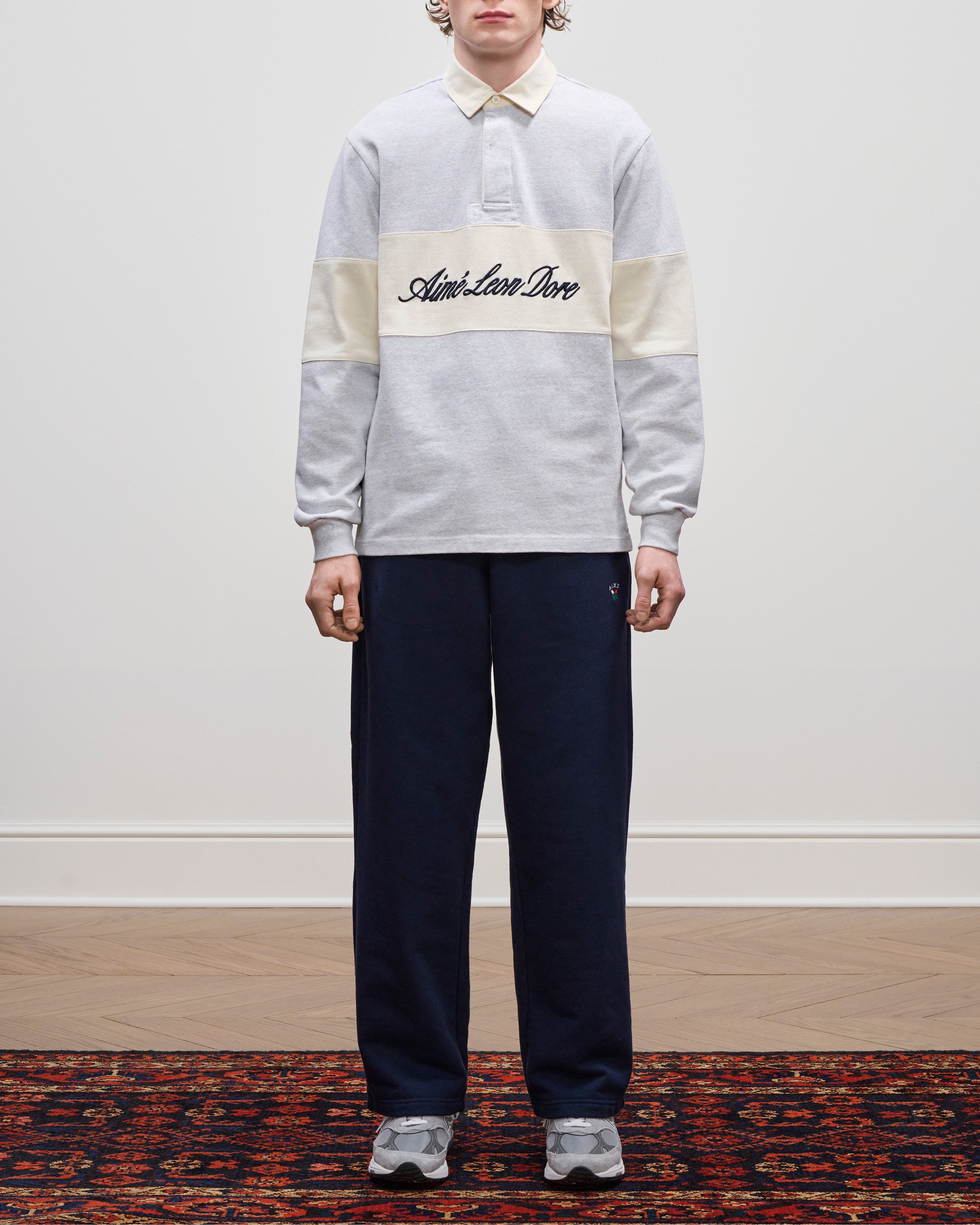 Person wearing the Script Paneled Rugby, navy pants, and grey sneakers, standing indoors.