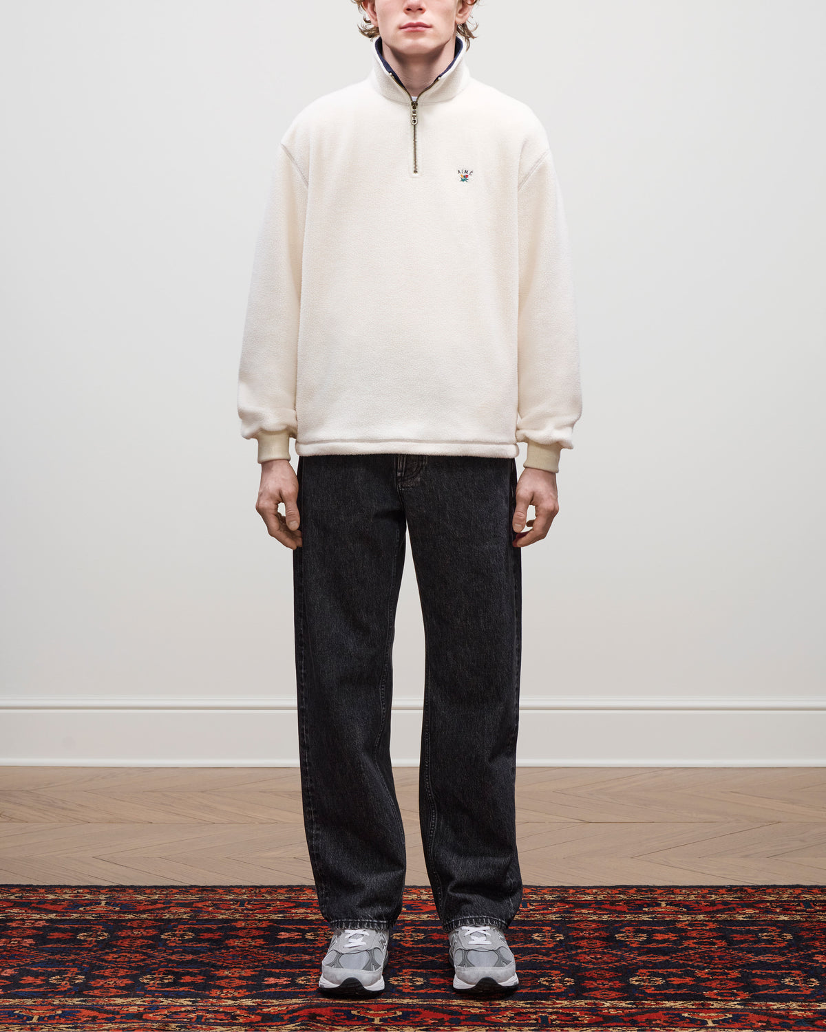 A person stands indoors wearing a Crest Quarter-Zip Fleece Pullover, dark jeans, and gray sneakers on a patterned rug.