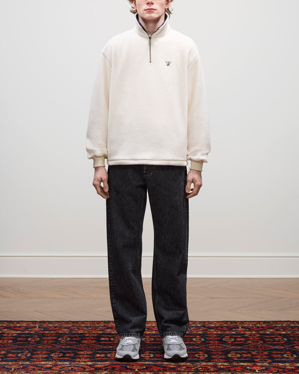 A person stands indoors wearing a Crest Quarter-Zip Fleece Pullover, dark jeans, and gray sneakers on a patterned rug.