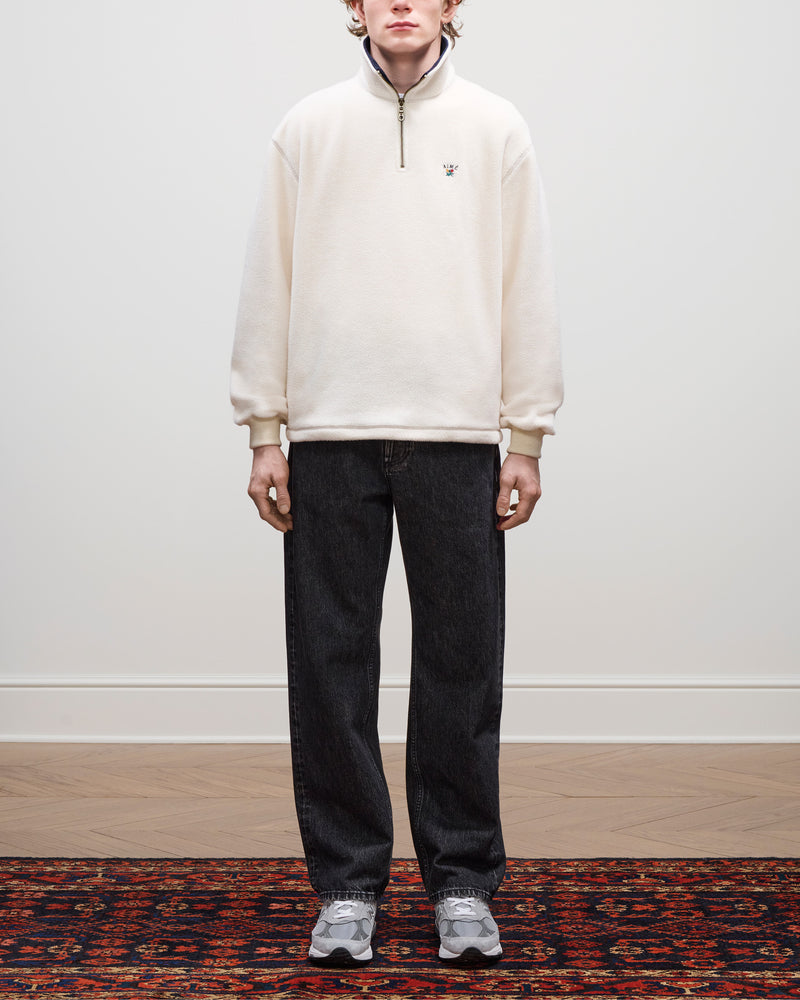 A person stands indoors wearing a Crest Quarter-Zip Fleece Pullover, dark jeans, and gray sneakers on a patterned rug.