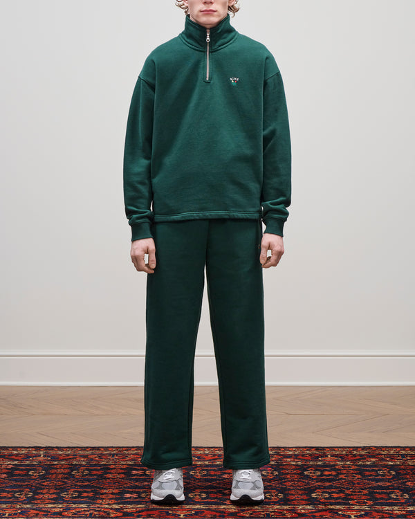 Person in Crest Sweatpants and gray sneakers stands on a patterned rug against a plain white wall.