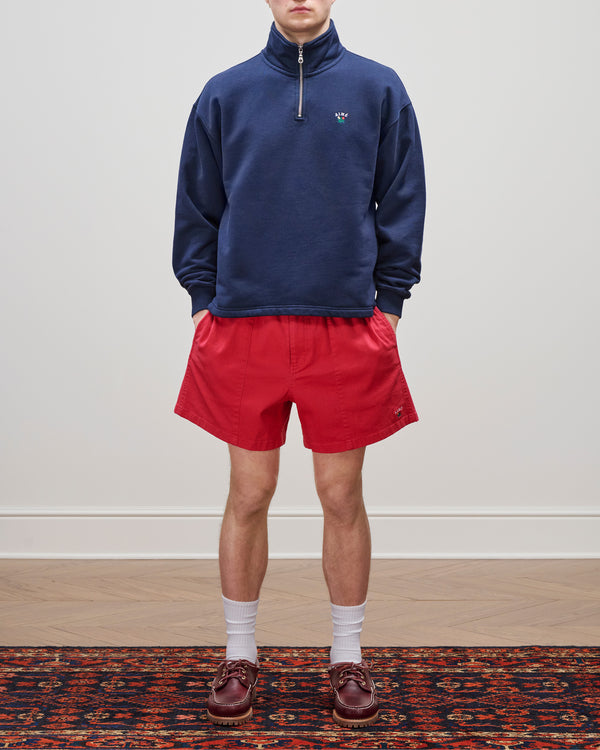 Wearing the Crest Quarter Zip Pullover in navy, red shorts, white socks, and brown loafers on a patterned rug.