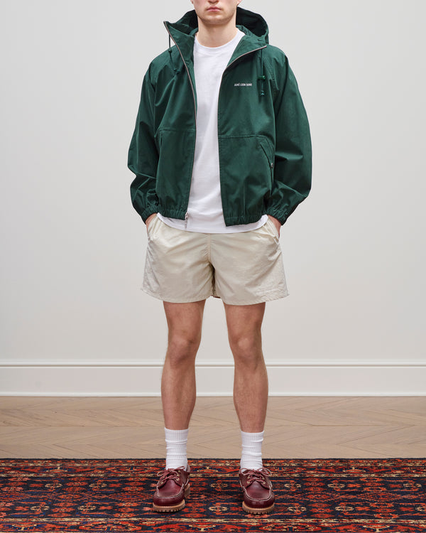 A person wearing Core Nylon Short, green jacket, white t-shirt, white socks, and brown shoes stands on a patterned rug.