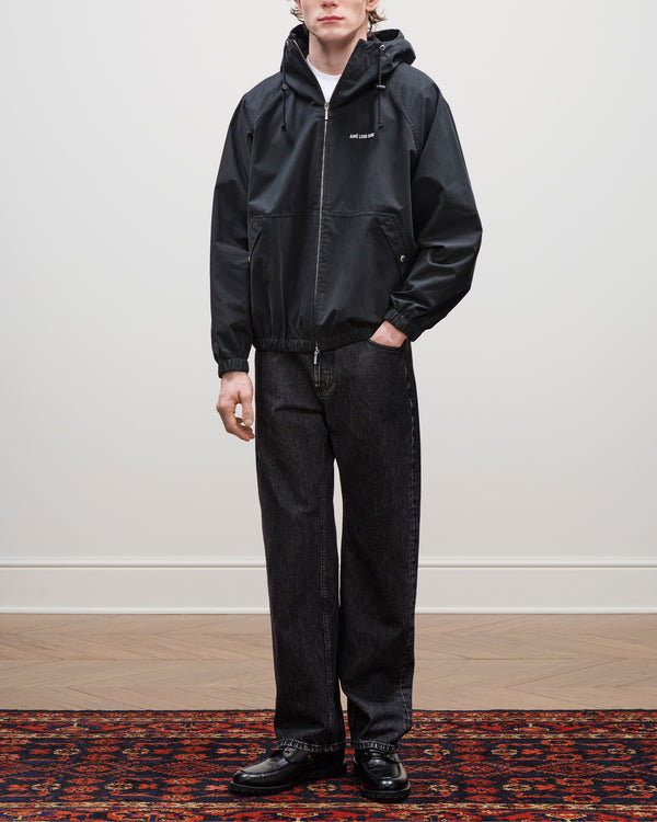 Person wears the Micro Logo Lightweight Jacket, dark jeans, and black shoes on a patterned rug against a plain wall.