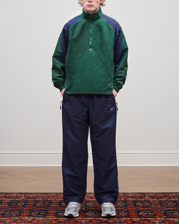 Person in a Crest Nylon Half-Zip Pullover with gray sneakers, on a patterned rug against a plain wall.