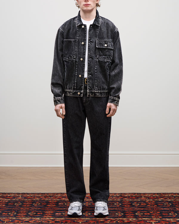 Person wearing a Denim Trucker Jacket, matching jeans, white shirt, and gray sneakers on a patterned rug.