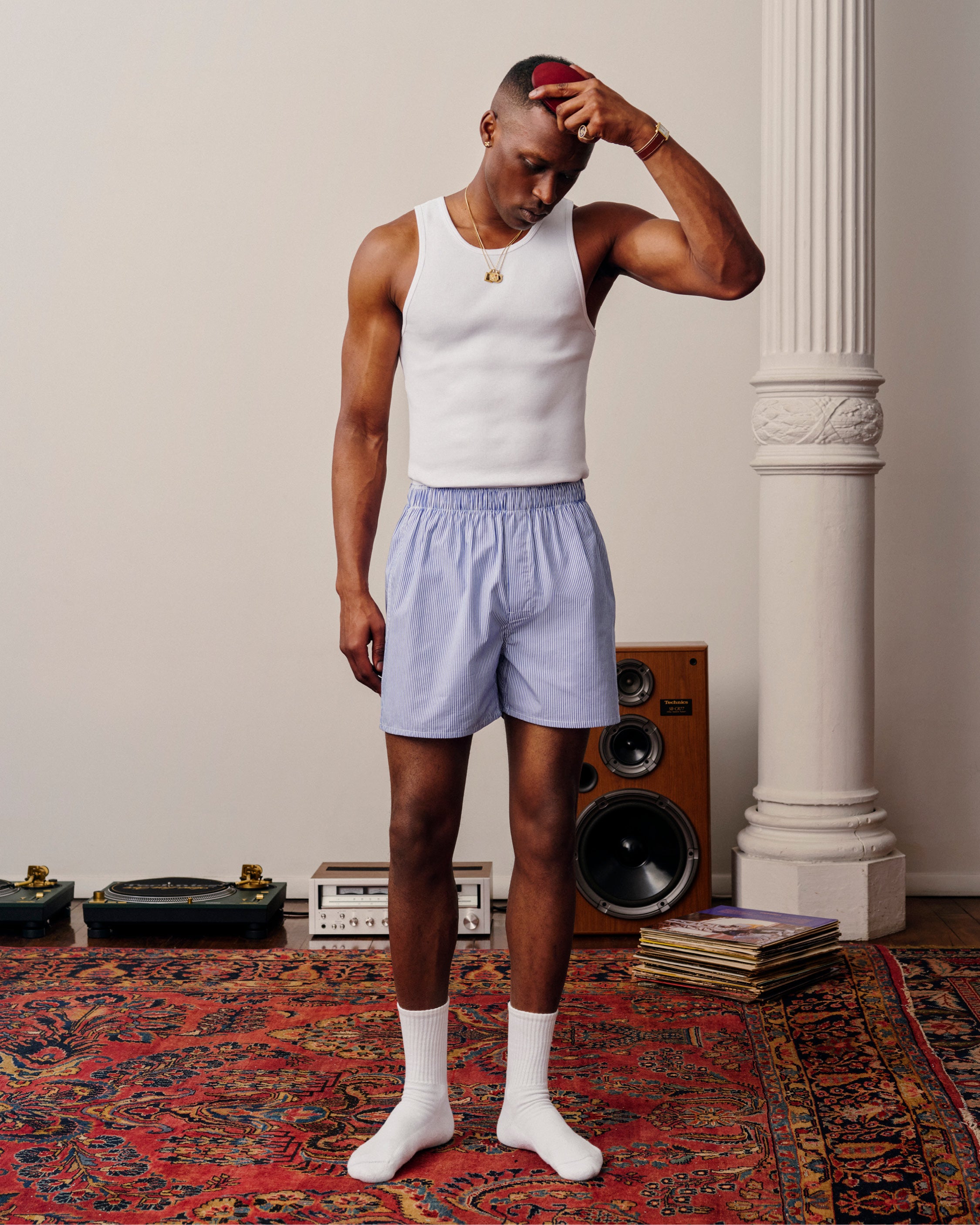 Man wearing Boxer Short 2-Pack stands on a patterned rug near speakers and vinyl records.