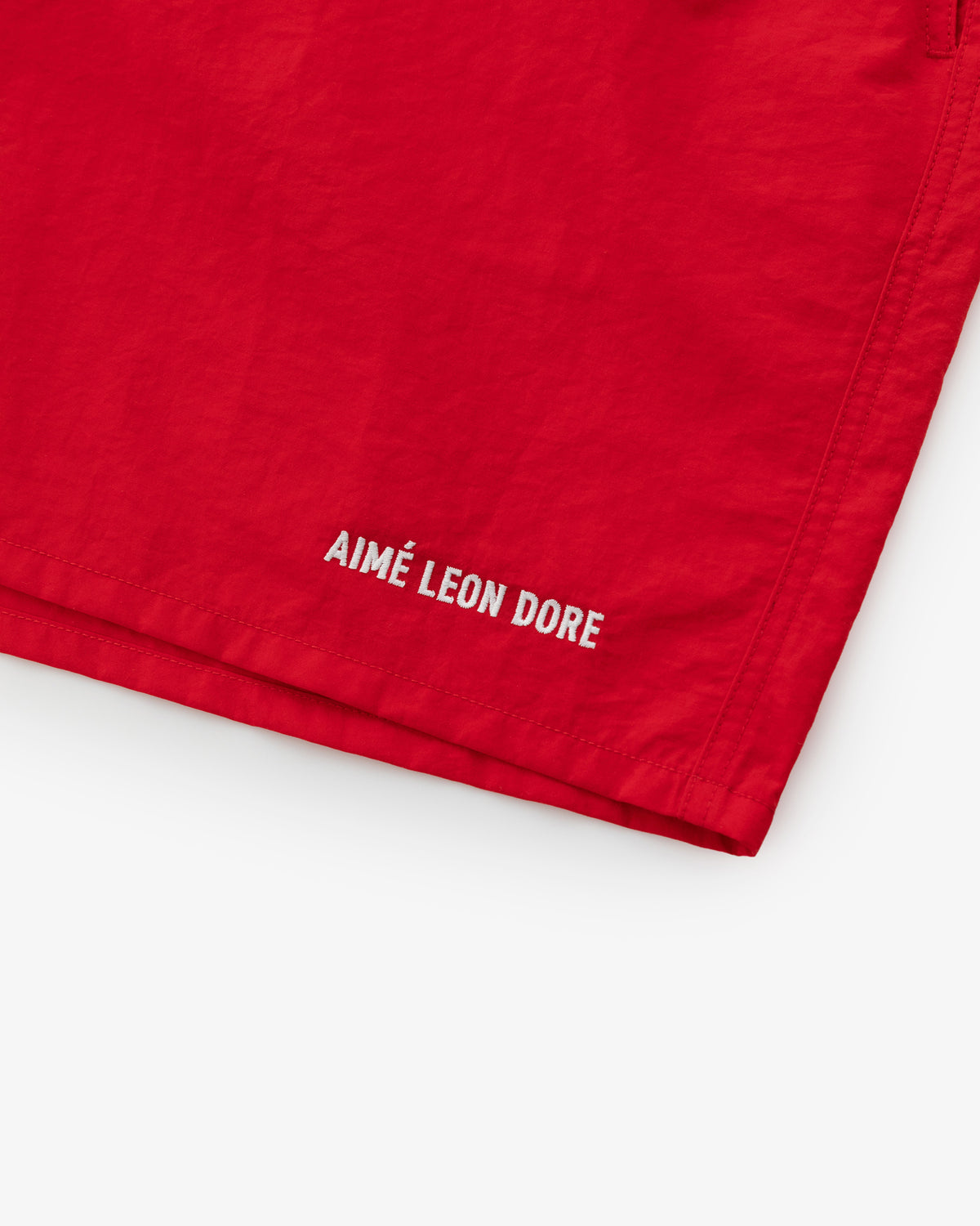 Close-up of Logo Swim Short in red with AIMÉ LEON DORE logo in white text near the hem.