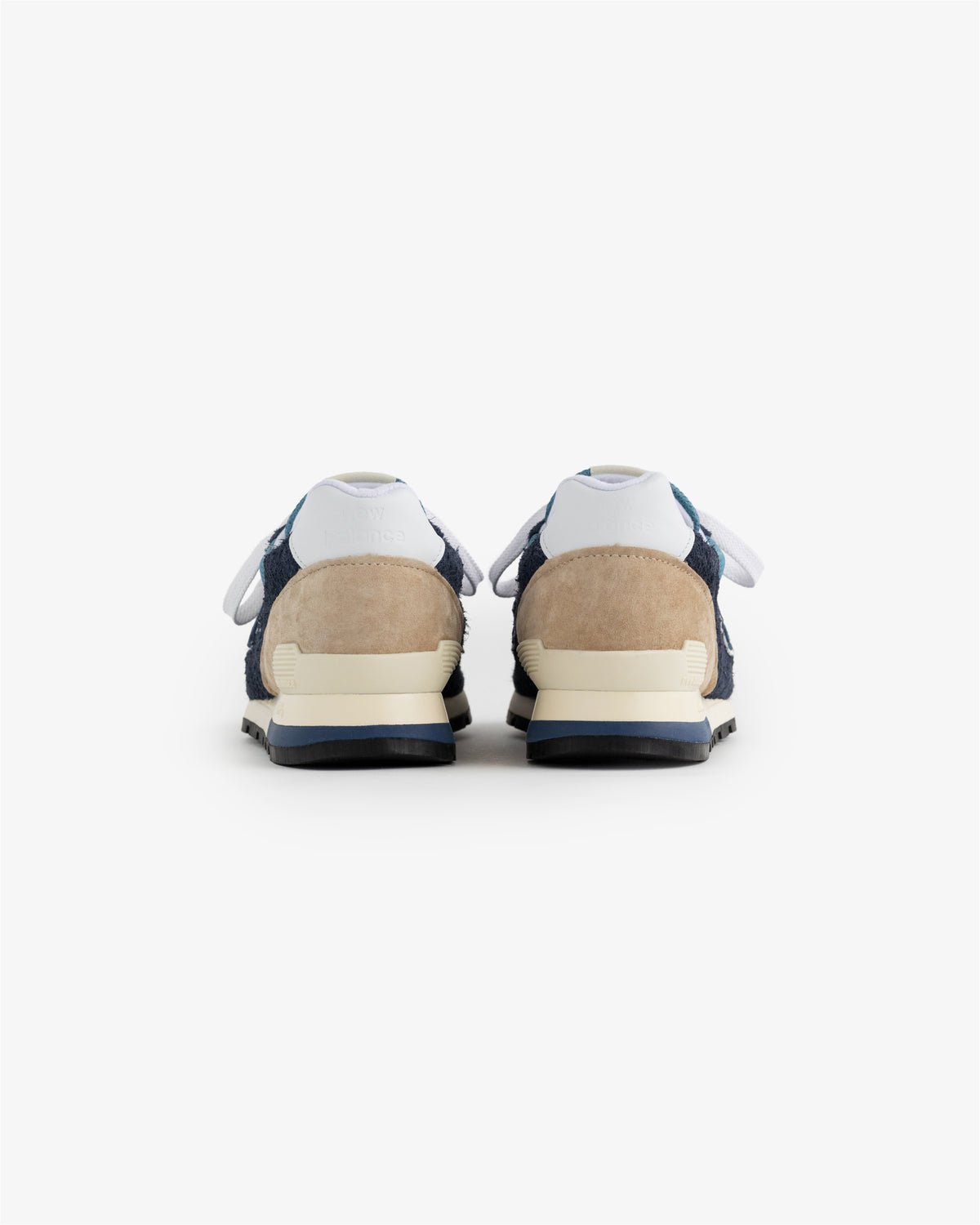 A pair of New Balance Made in USA 996 sneakers in navy, beige, and white shown from the back on a white background.