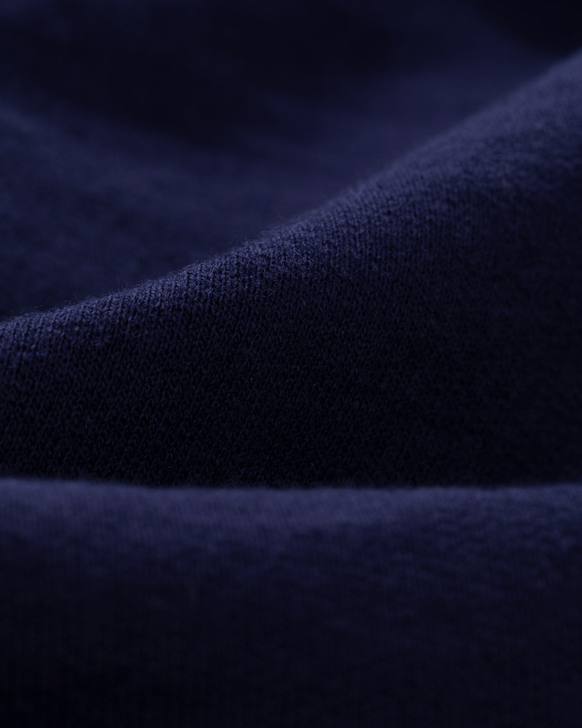 Close-up of Tonal Logo Sweatshorts in dark blue, highlighting soft folds and visible fabric texture.