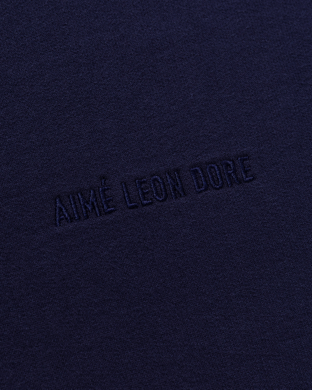 Close-up of dark blue Tonal Logo Sweatshorts with AIMÉ LEON DORE embroidered in matching blue thread.